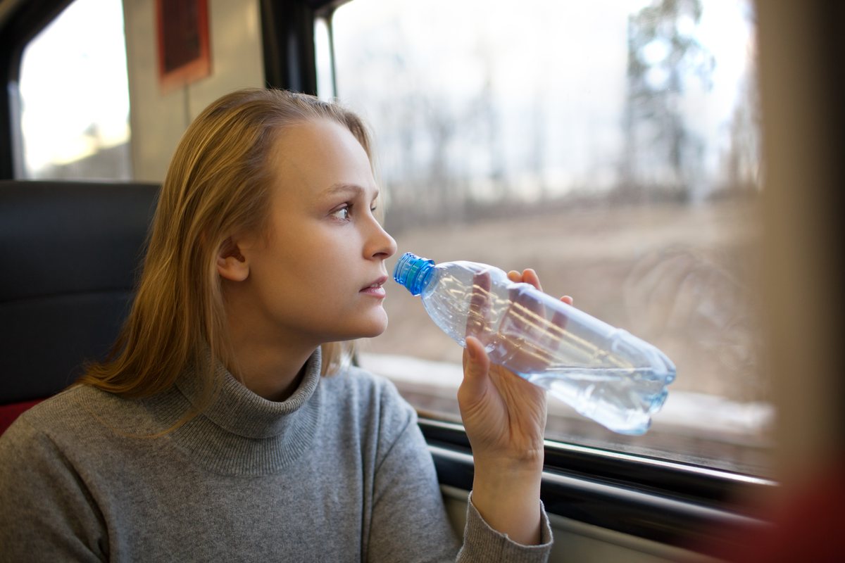 Fahrgast trinkt im Zug Wasser aus einer Flasche und schaut aus dem Fenster